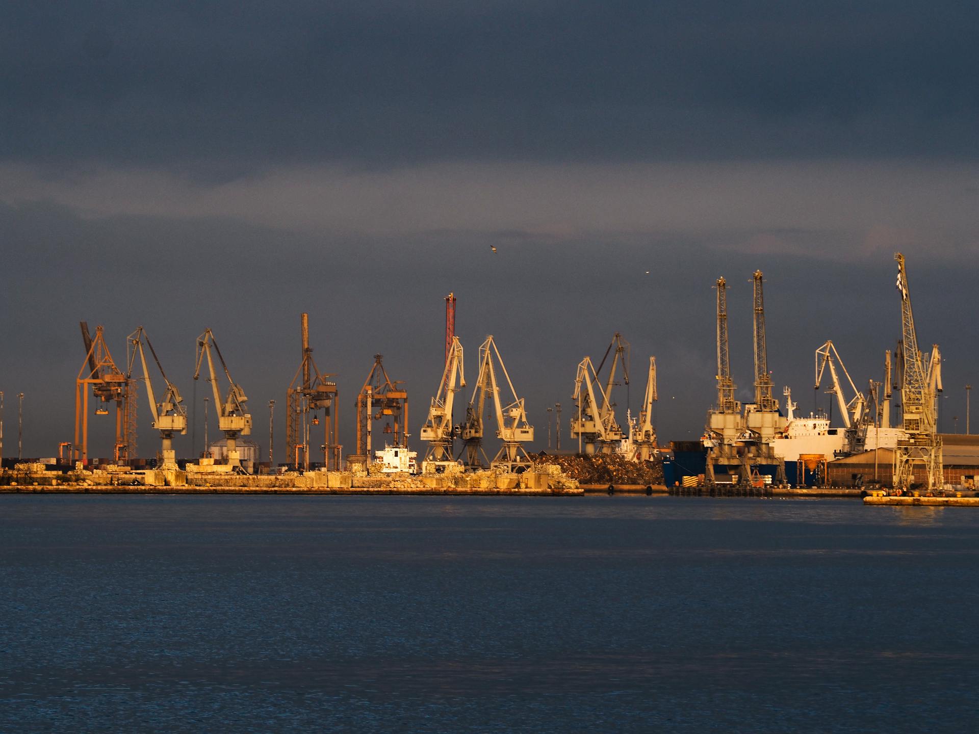 A serene view of a bustling cargo port at sunset, featuring cranes and ships.