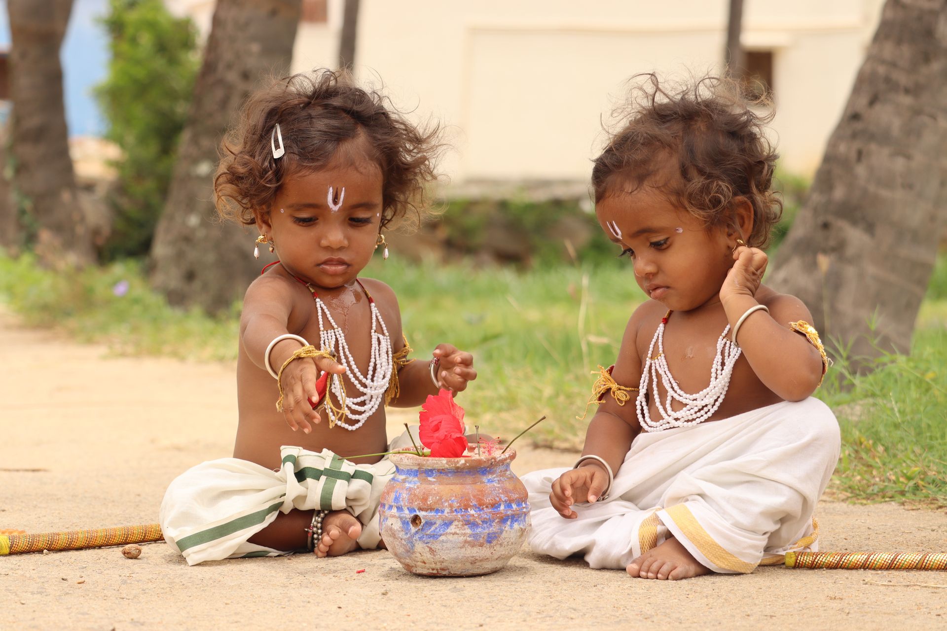 Two South Asian toddlers in traditional dress playing together outdoors in Kuppam, India.