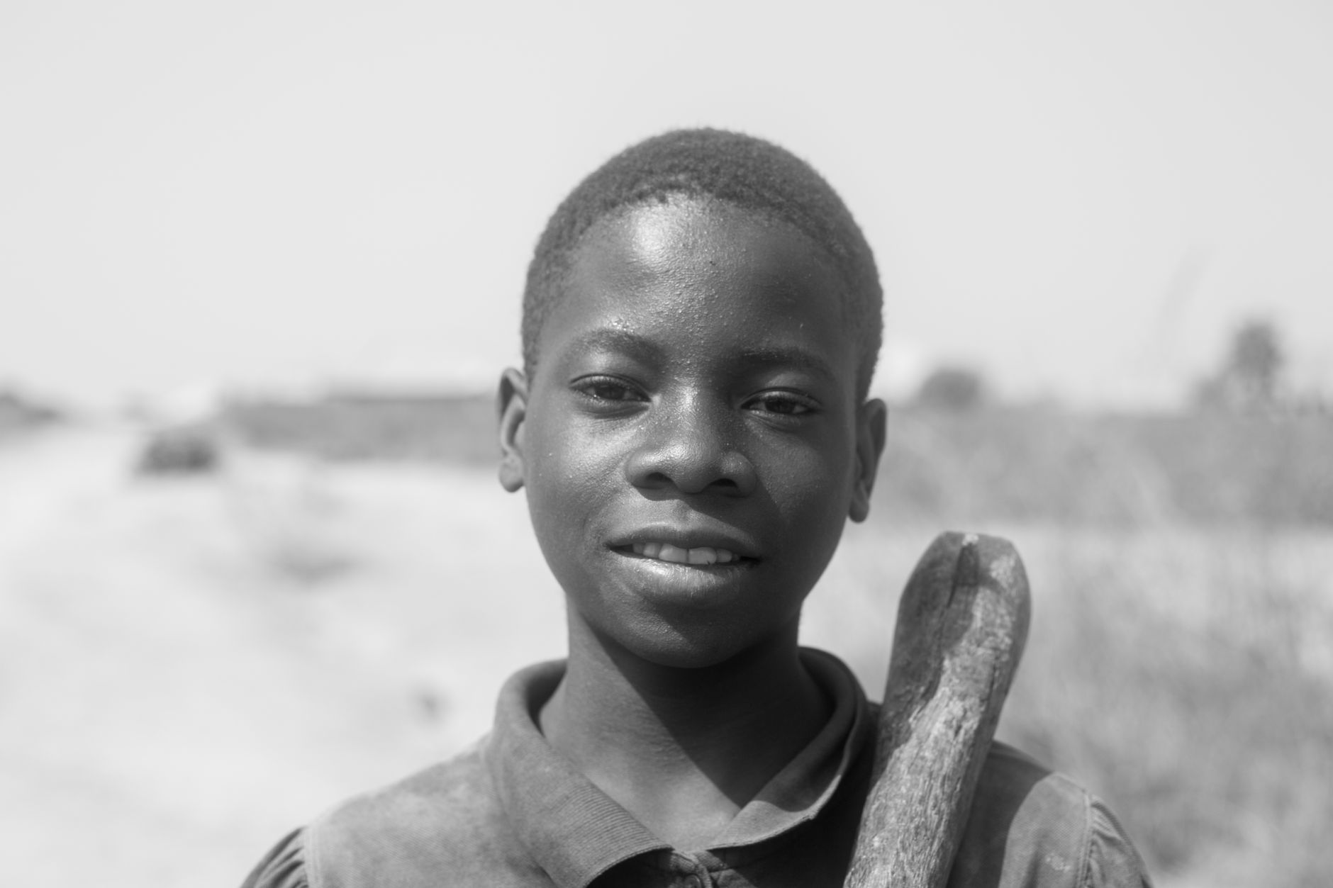 Black and white portrait of a smiling boy outdoors in rural Kaduna, Nigeria.