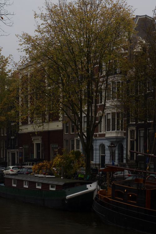 Free Serene view of Amsterdam canal with historic buildings and traditional houseboats on an overcast day. Stock Photo