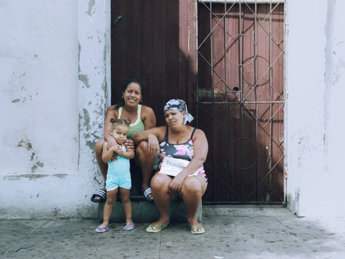 Free Three generations of women sitting by a doorway in an urban environment, expressing community. Stock Photo
