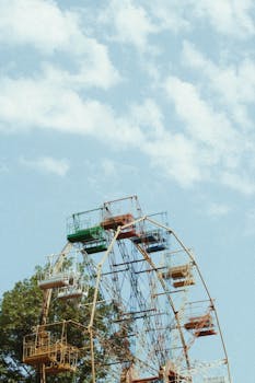 A vintage Ferris wheel with colorful cabins set against a bright blue sky and scattered clouds.