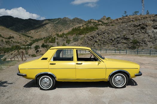 Classic yellow vintage car parked on a scenic mountain road under a blue sky.