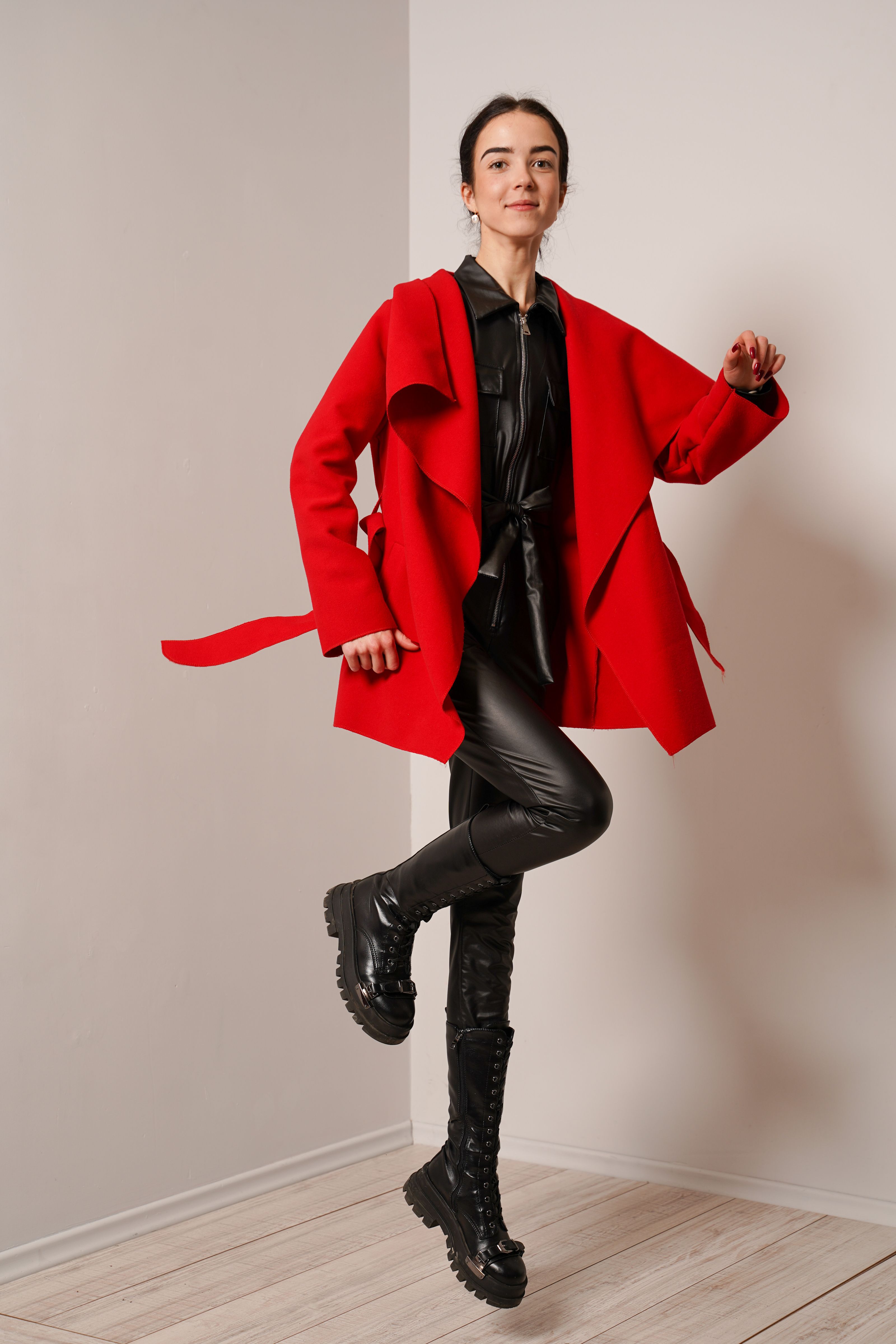 Mulher fashionista em casaco vermelho e roupa de couro preto posando dentro de casa.