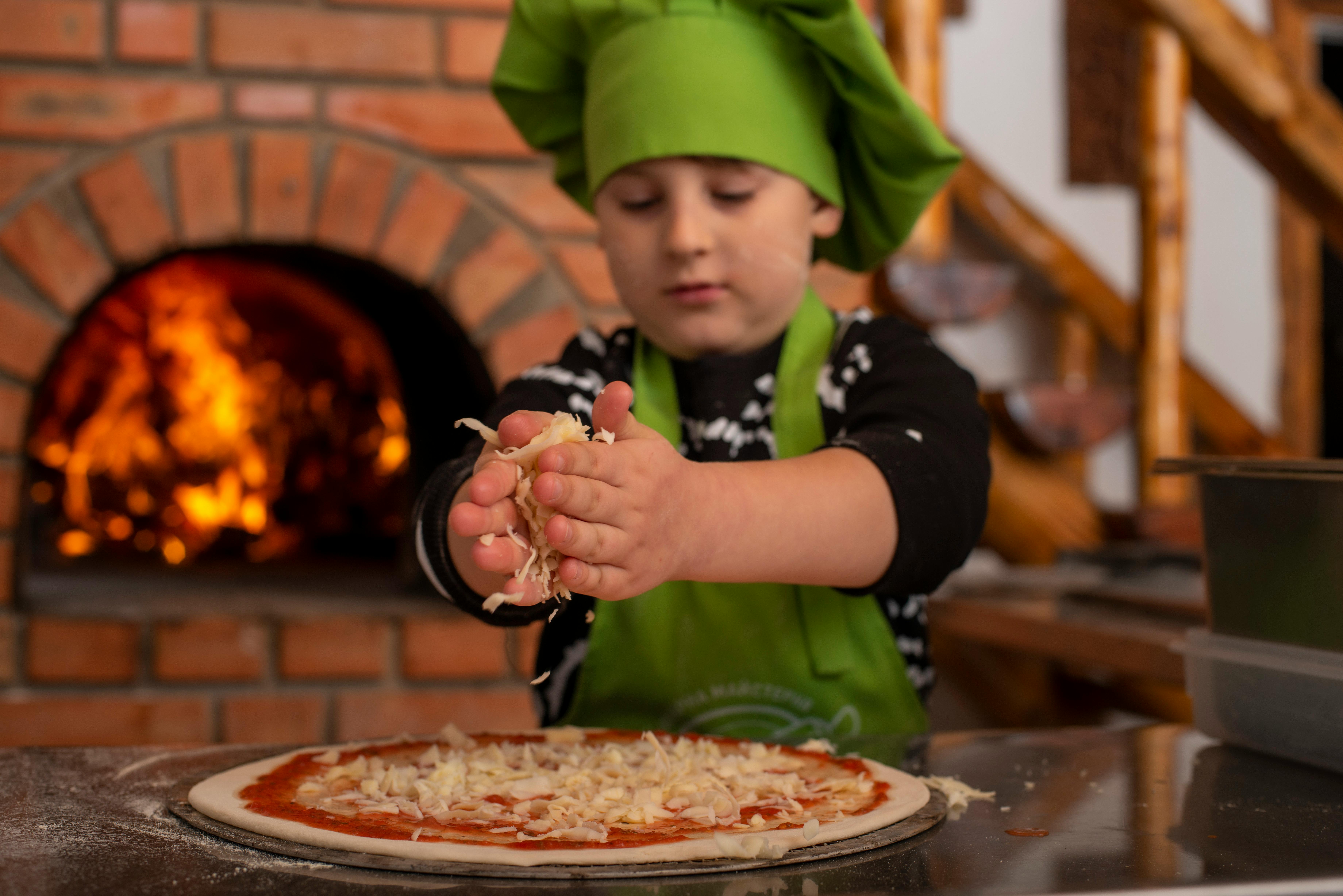 a young boy in green apron making pizza