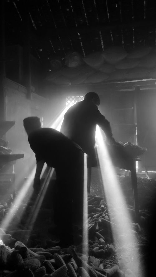 Free Black and white image of workers silhouetted against beams of light in a workshop setting. Stock Photo