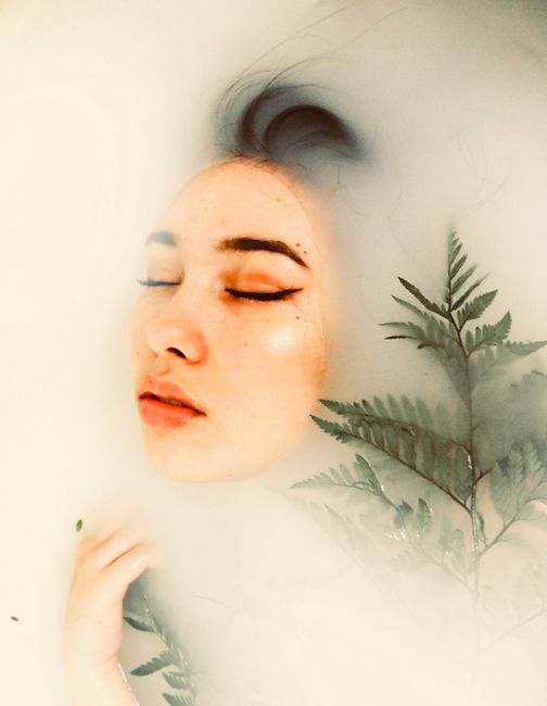 Tranquil face of a woman submerged in milky water, surrounded by ferns.