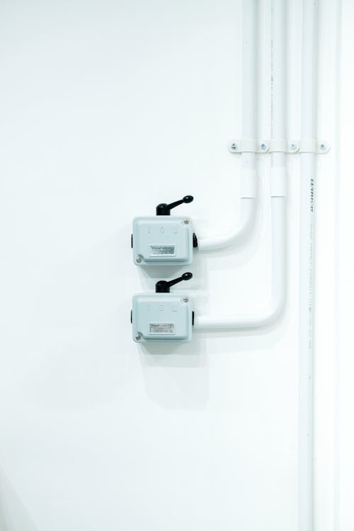 Free Clean and modern electrical switches mounted on a white wall with piping. Stock Photo