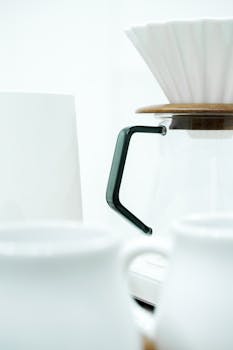 Close-up of a minimalistic coffee pour over setup with white ceramic mugs and a glass pitcher.