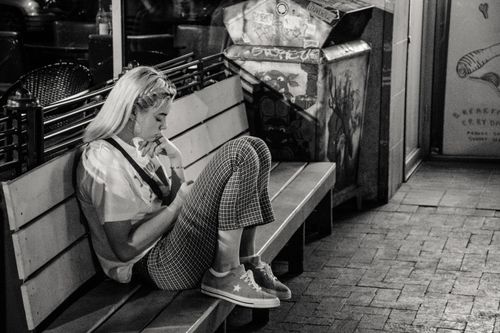 Free Black and white photo of a young woman seated alone on a street bench at night. Stock Photo
