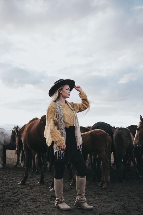 Free A stylish woman in a cowboy hat stands with a herd of horses on a cloudy day. Stock Photo