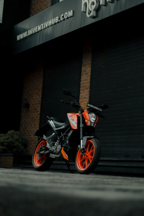 Free A sleek motorcycle with vibrant orange accents parked outside a brick industrial building in India. Stock Photo