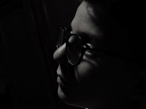 Close-up black and white profile of a boy wearing glasses, dramatic shadows.