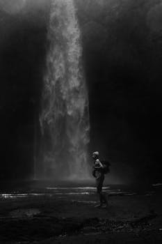 A lone adventurer stands near a waterfall in Bali, captured in dramatic monochrome.