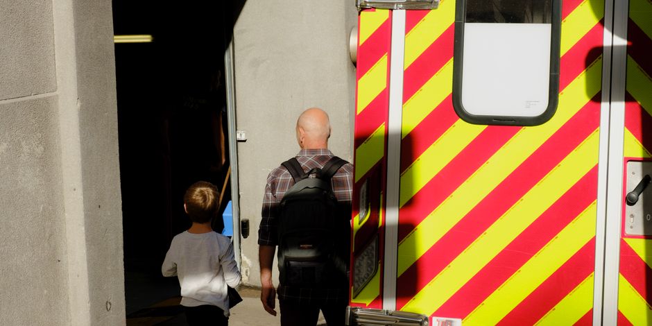A man and a child entering a building beside a brightly colored ambulance.