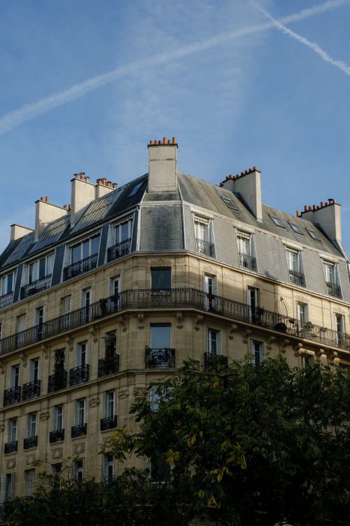 Free Corner view of a classic Parisian building with clear blue skies and lush greenery. Stock Photo