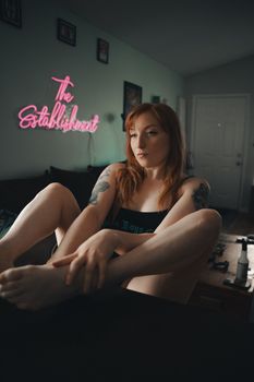 A redhead woman with tattoos sitting relaxingly in a room with stylish decor.