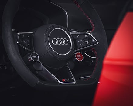 Close-up of a luxury car steering wheel featuring the Audi emblem and control buttons.