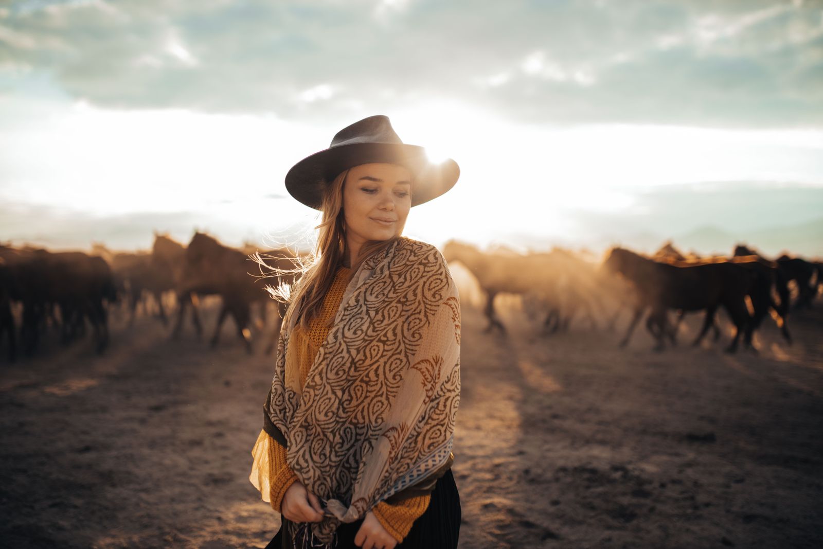 Mulher country ao pôr do sol com cavalos ao fundo