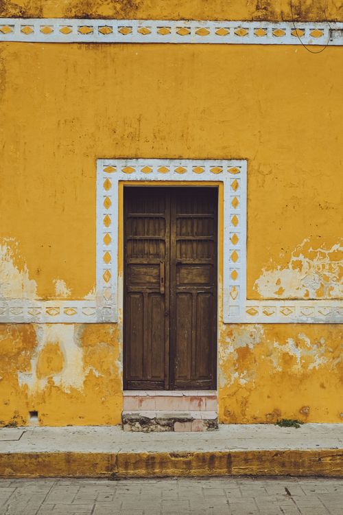 Free A rustic wooden door set in a vibrant mustard yellow wall with decorative trim. Stock Photo