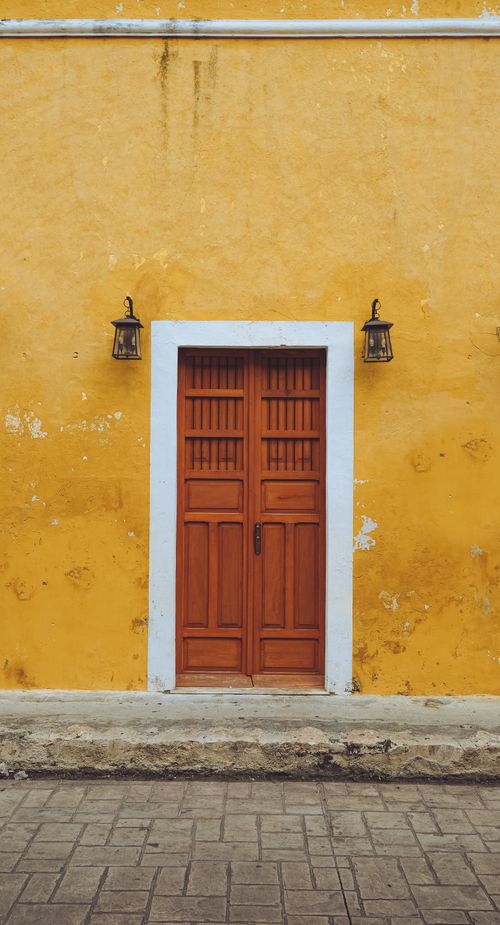 Free Capture of a wooden door on a vibrant yellow wall with vintage lanterns. Stock Photo