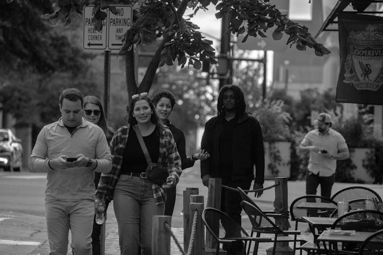 Grayscale Photo Of Friends Walking On Sidewalk