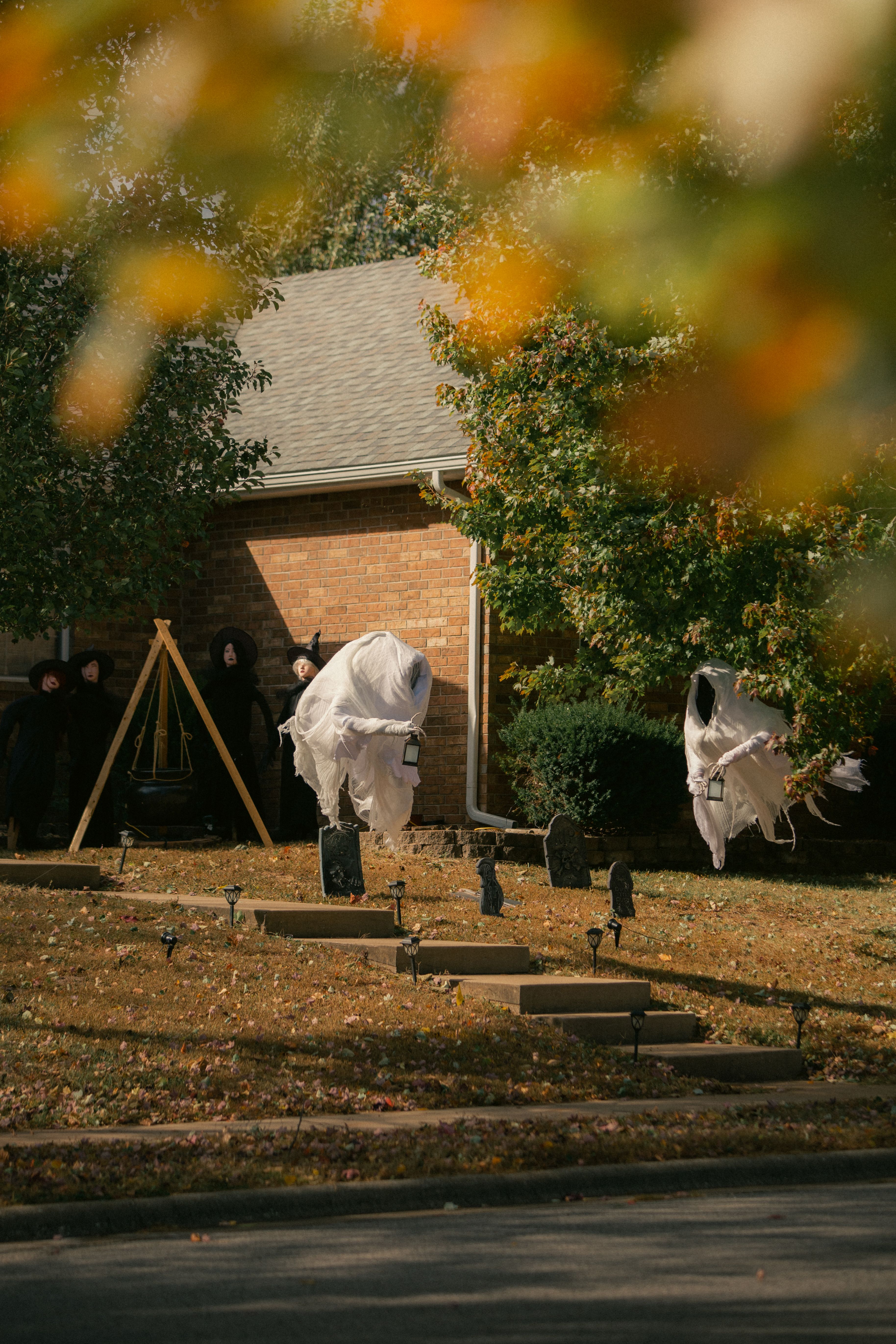 Ghost decorations in a fall front yard create a Halloween ambiance.
