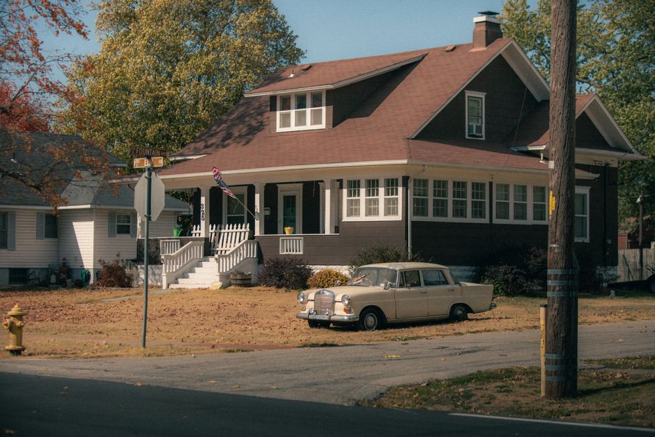 Classic beige car parked by a charming vintage house in a quiet residential area.