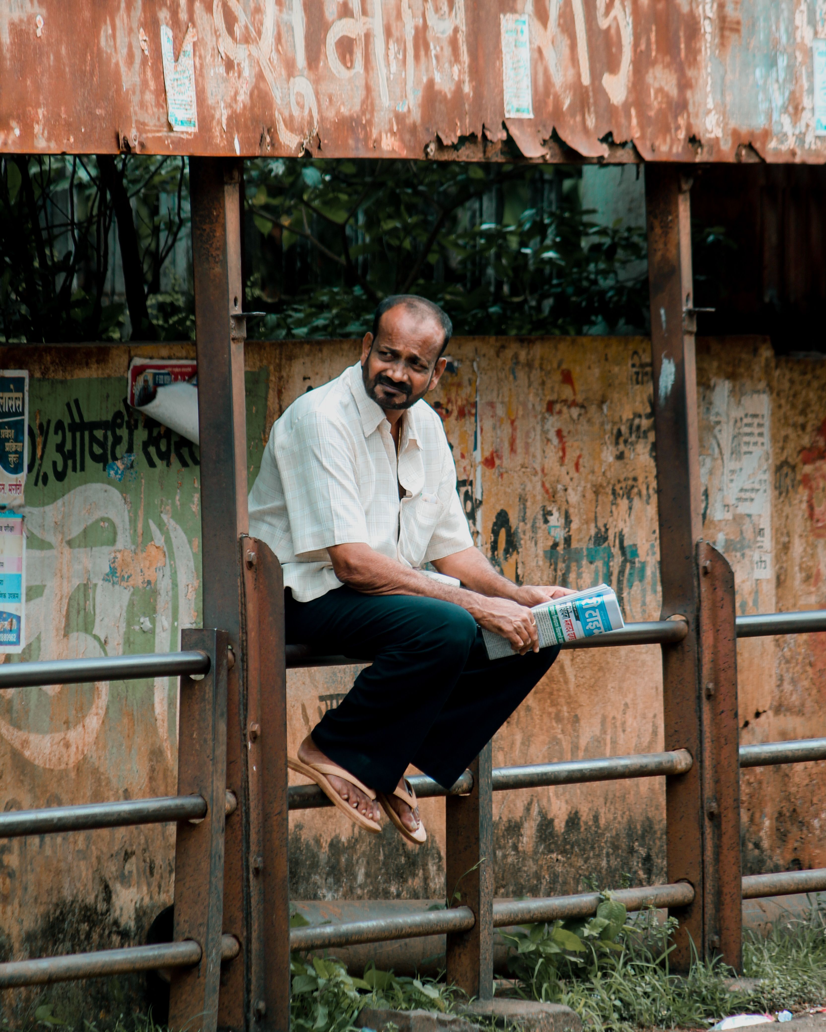 A man reading a newspaper while sitting at a bus stop in Ratnagiri, Maharashtra, India.