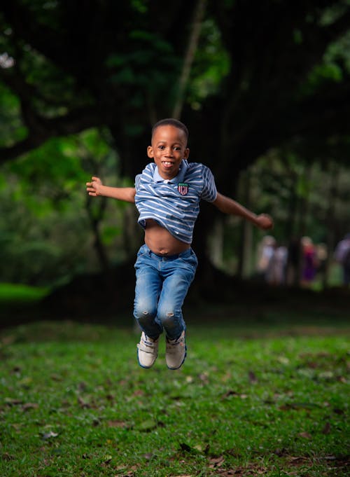 Boy in Stripe Shirt Jumping on Grass