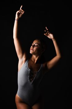 Graceful dancer in a bodysuit strikes a pose against a dark background, showcasing elegance and strength.