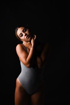 Studio portrait of a dancer posing gracefully in a gray bodysuit against a dark background.