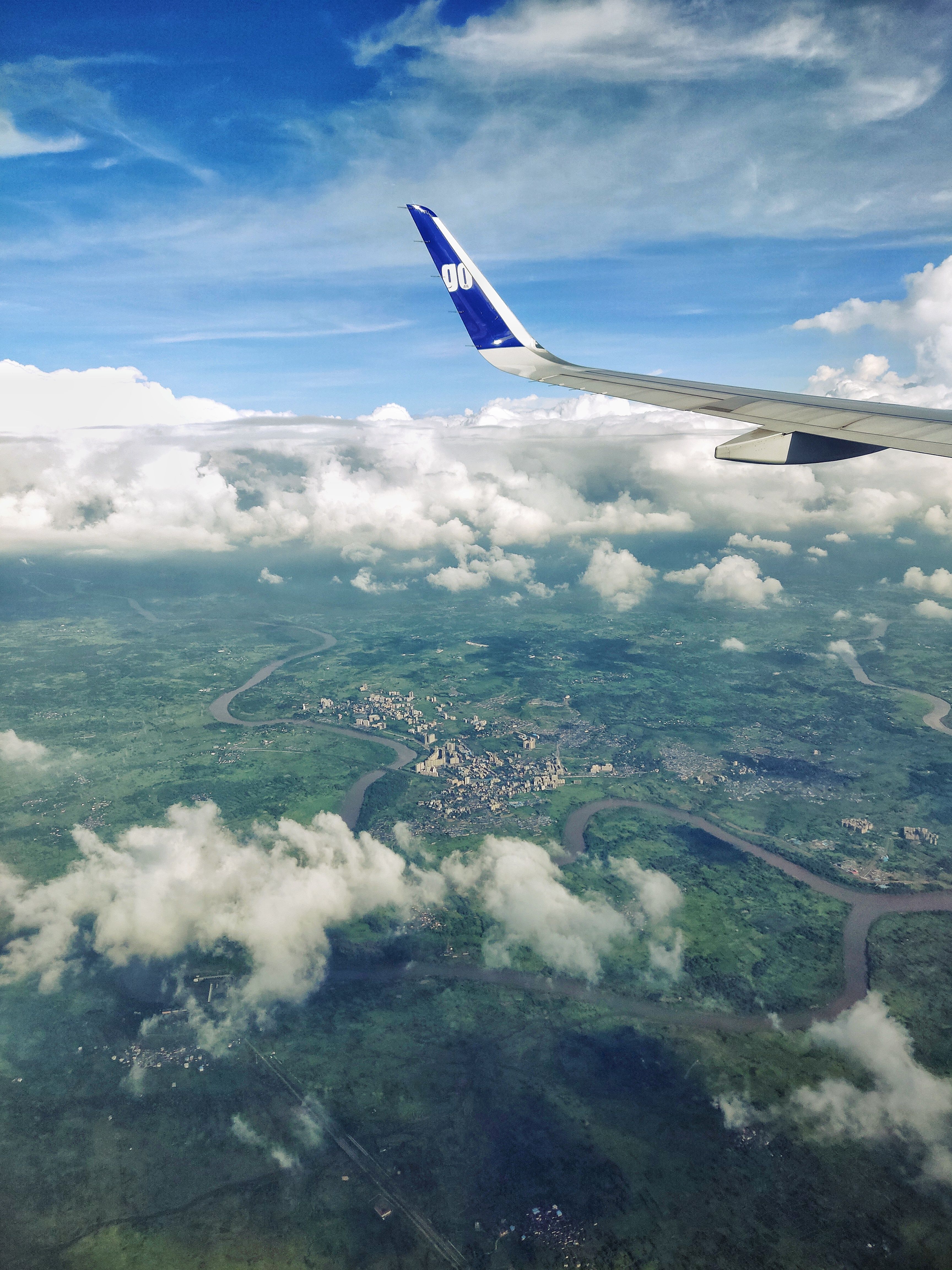 Scenic aerial view of Mumbai showing clouds, landscape, and airplane wing.