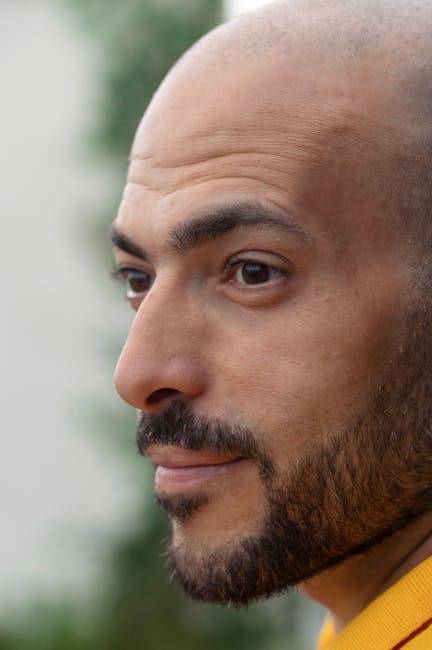 Side profile close-up of a bald man with a beard, face focused on the outdoors.