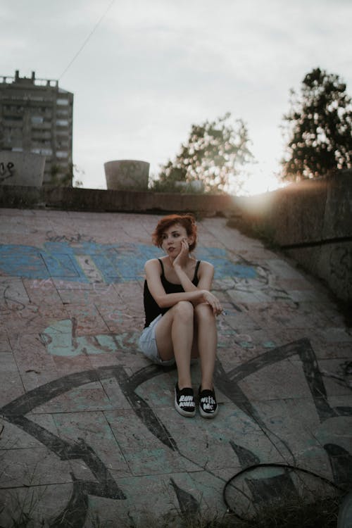 Free Woman Wearing Black Tank Top Sitting on Concrete Surface Stock Photo
