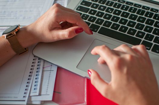 Close-up of a woman's hands typing on a laptop with red manicured nails and wristwatch.