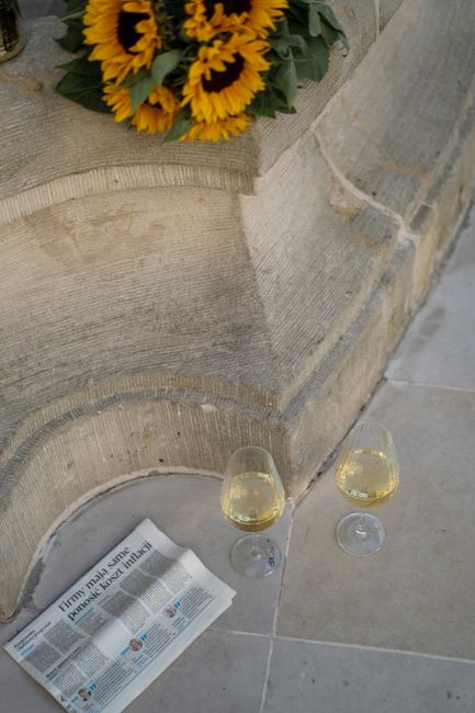 Bouquet of sunflowers, two glasses of white wine, and a newspaper on a tiled floor.