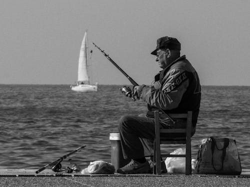 Grayscale Photo of Man Holding a Fishing Rod
