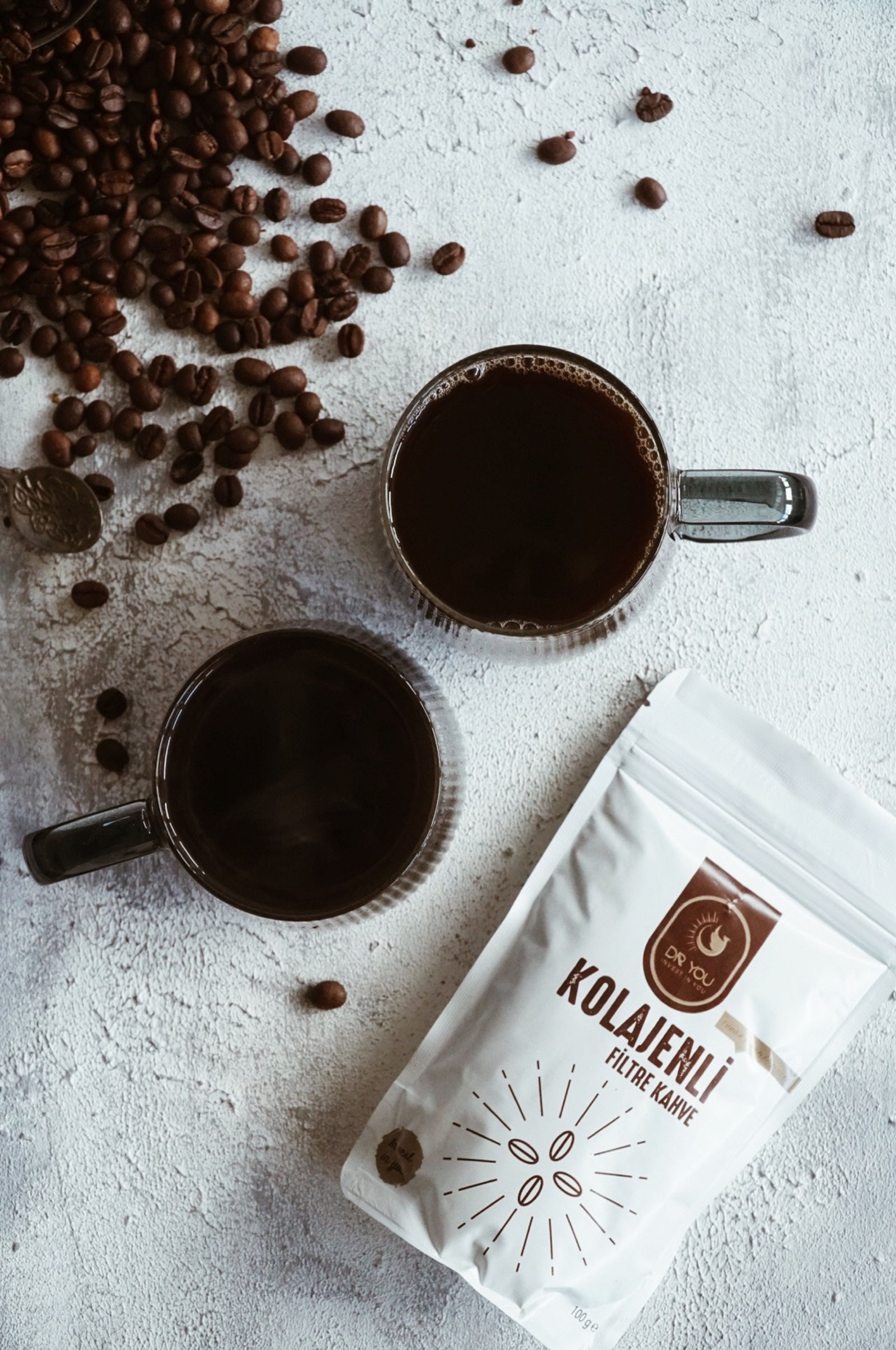 Coffee cups and beans on a textured surface with packaging, top view.