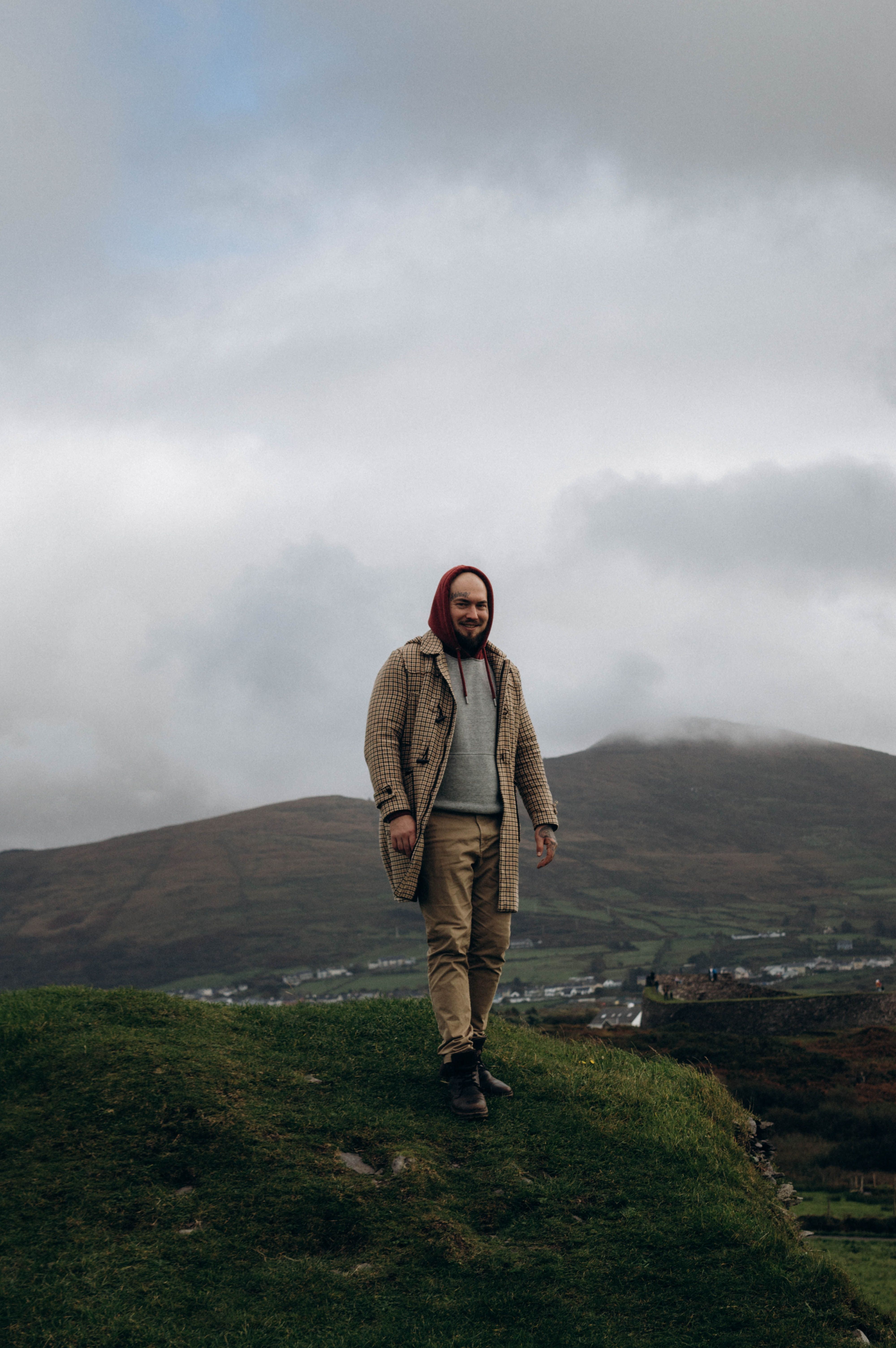 A man smiles while standing in a foggy countryside landscape with mountains.