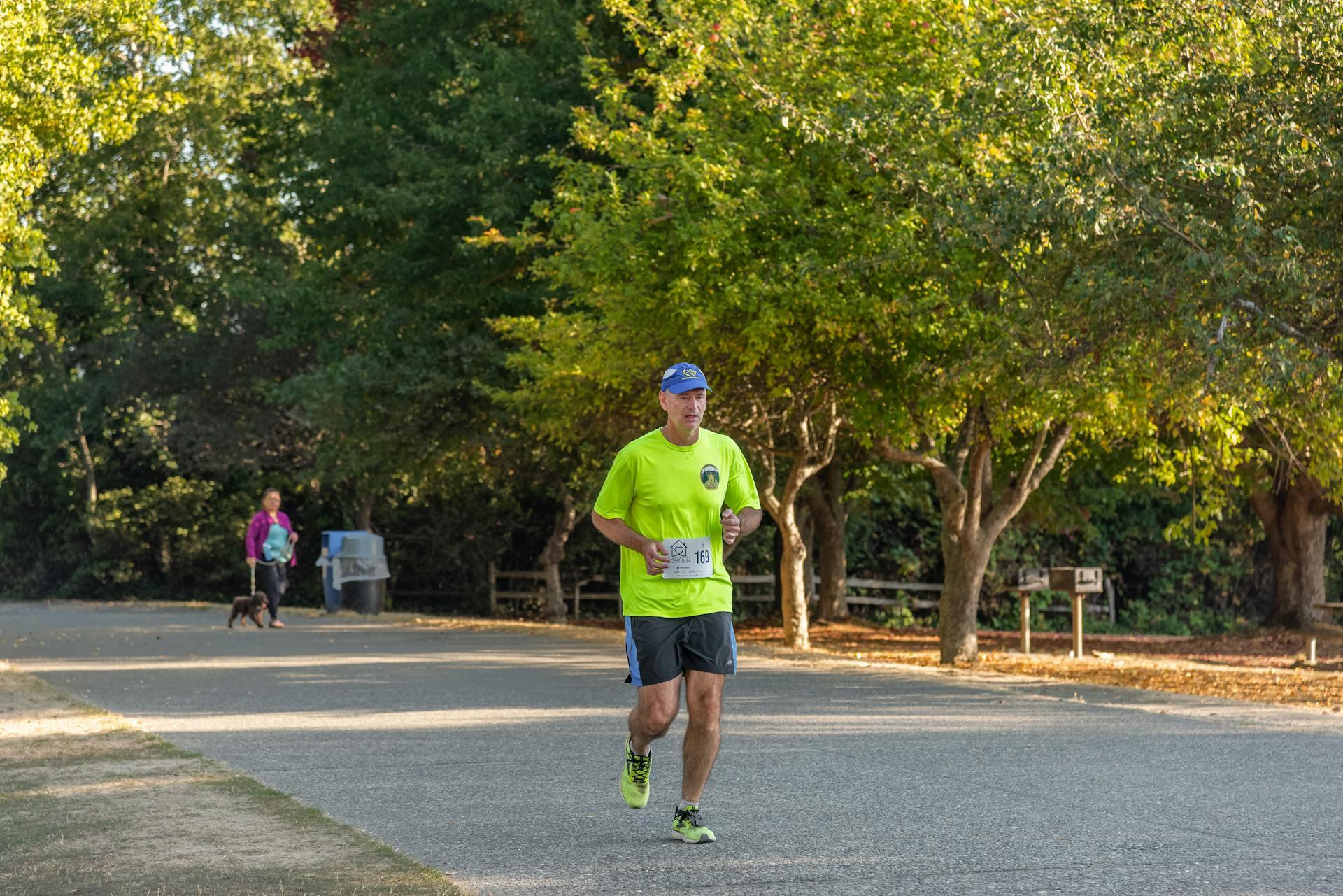 Man in Green Nike Crew Neck T-shirt and Black Shorts Running on Gray Concrete Road