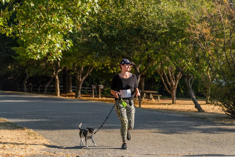 Woman Running In A Park With Her Dog On A Leash 