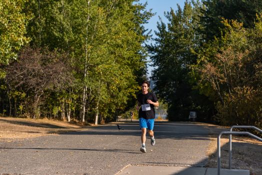 A young man participates in a marathon through a sunlit park, showcasing outdoor fitness and recreation.