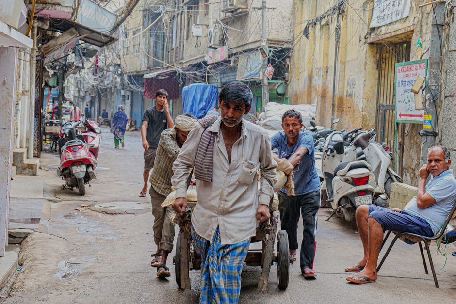 Candid capture of street workers pushing a cart in the bustling streets of Old Delhi, India.