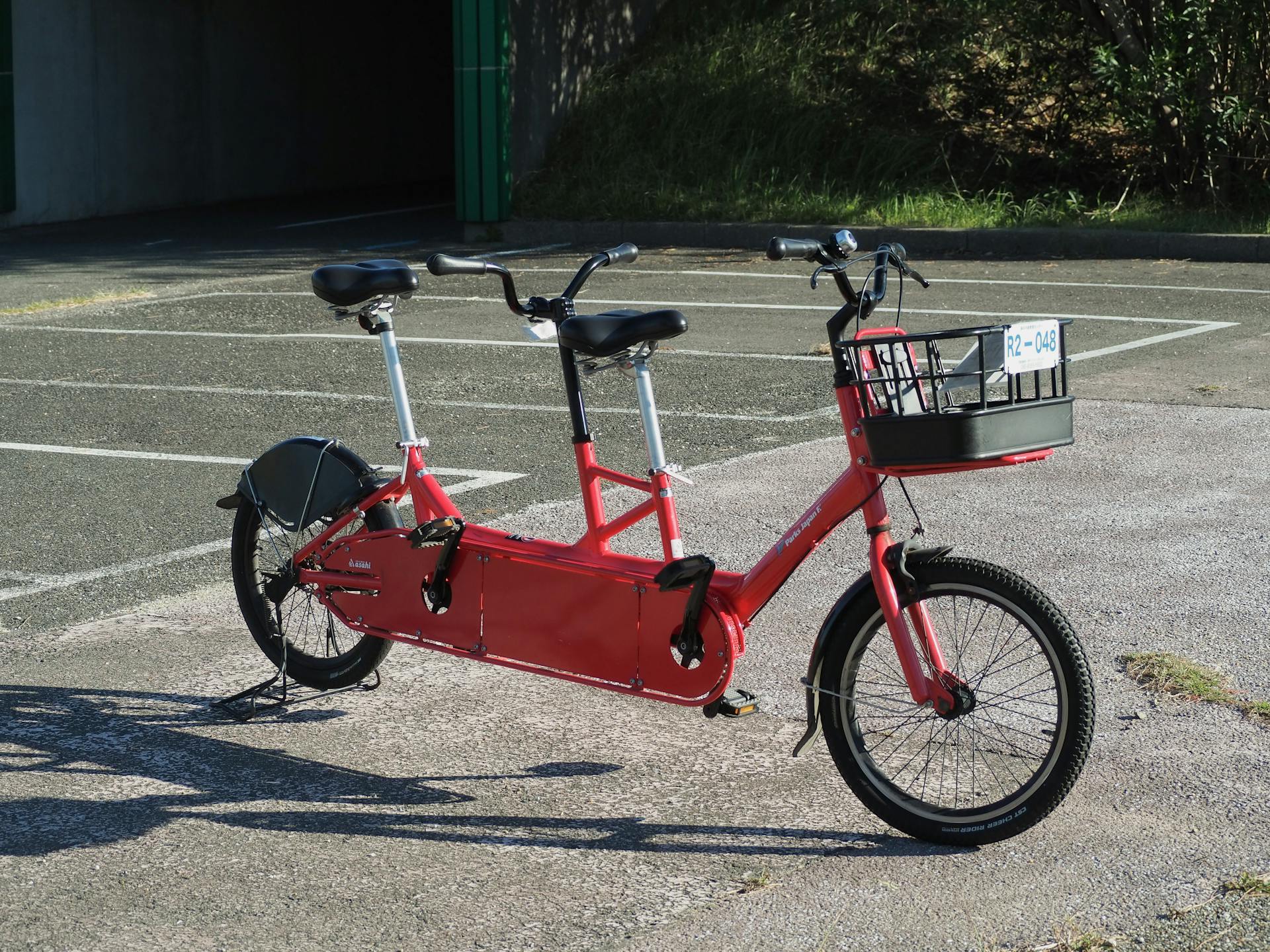 Red tandem bicycle parked in a sunny outdoor area, ideal for transportation and recreation imagery.