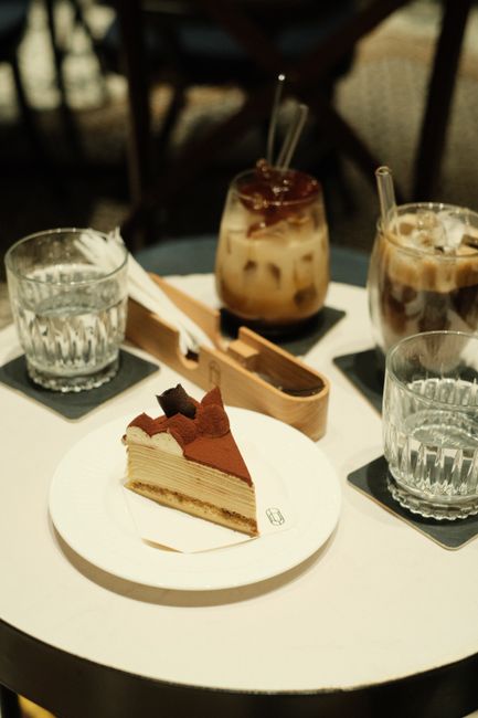 Slice of layered cake with coffee on table in cozy cafe setting.