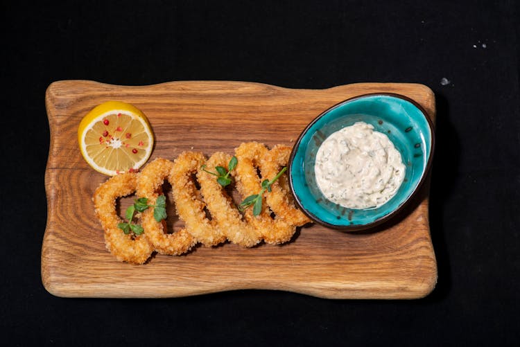 An Onion Rings On A Wooden Board With Dip On The Side