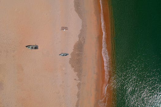 航拍镜头展现了沙滩上的船只和清澈的绿色海浪，突显了夏季的海滨景观