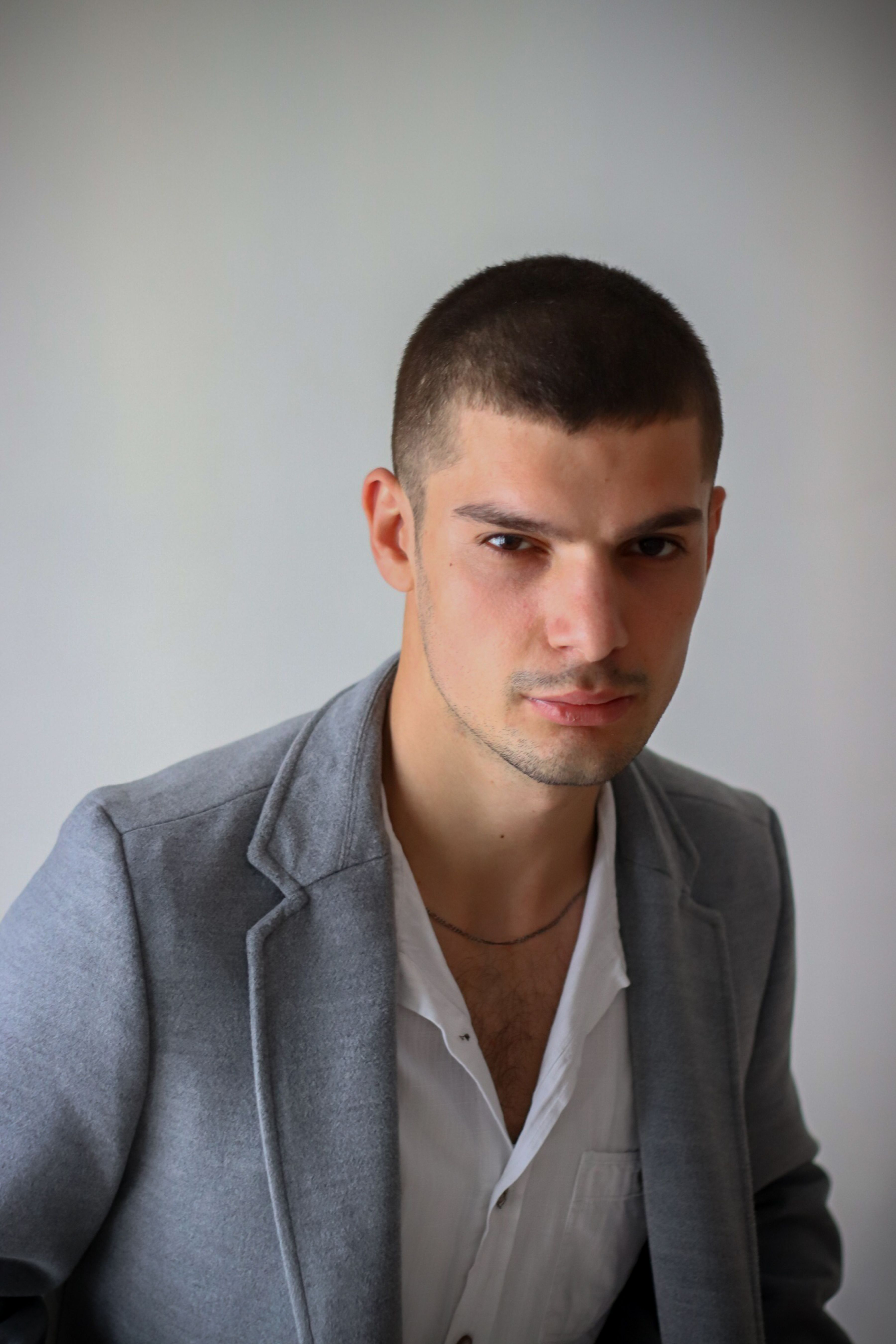 Portrait of a serious young man in a gray suit taken indoors in a studio setting.