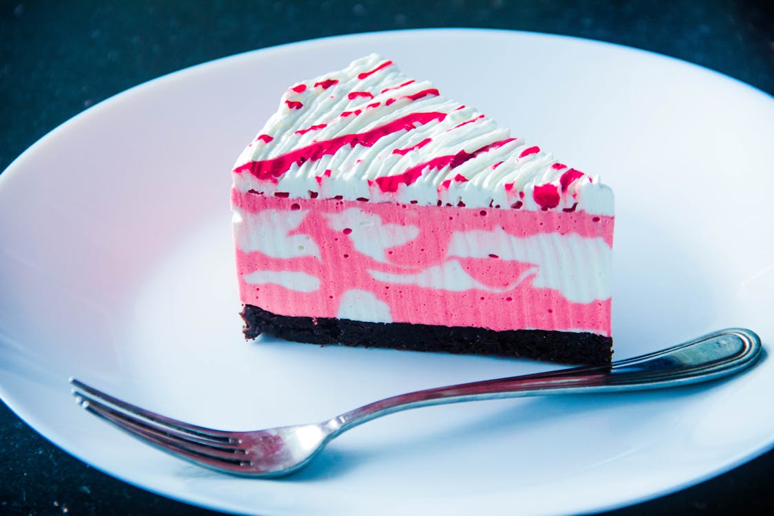 Sliced White and Pink Icing Covered Cake on White Plate With Silver-colored Fork